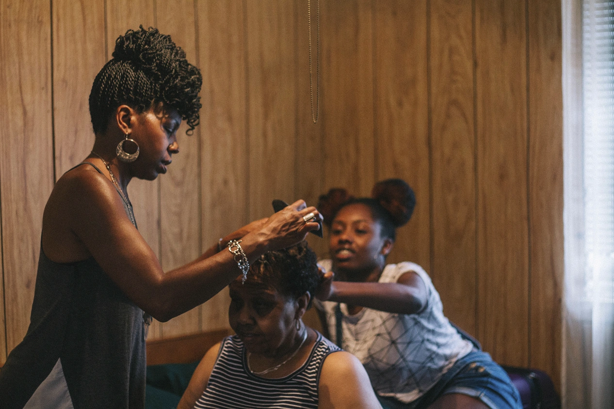 Three generations of women styling an older woman’s hair in a wood-panelled room