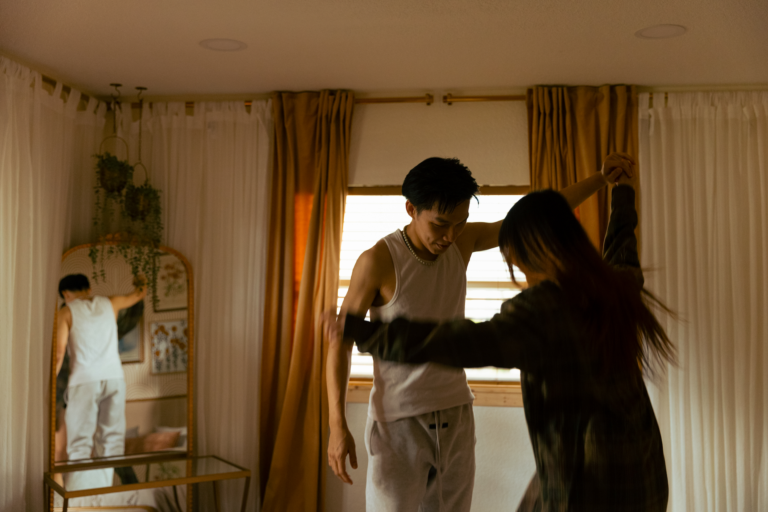A couple dancing together in a room framed by white and beige curtains with a gold mirror in the corner.