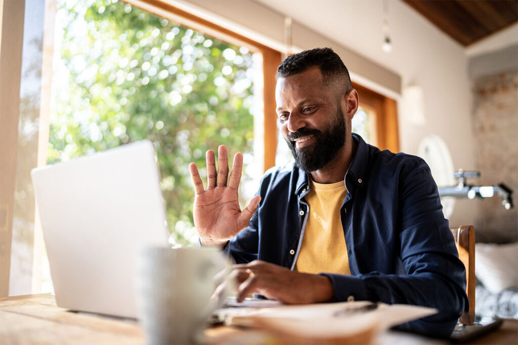 A man waving to his computer camera, starting an online therapy session