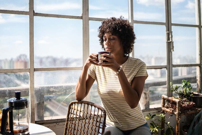 A perimenopausal woman sits at a small table sipping coffee
