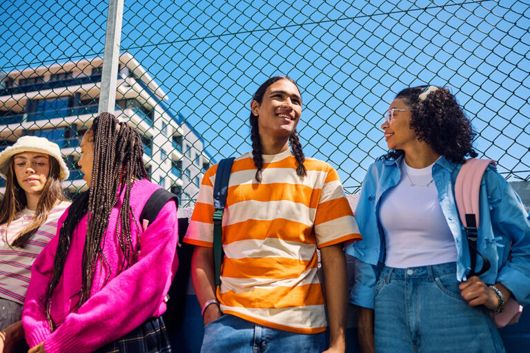 Four Gen Z friends lean against a fence while talking