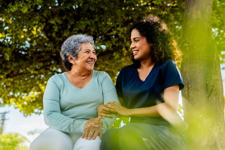 A young woman caregiver sits outside with her elderly loved one