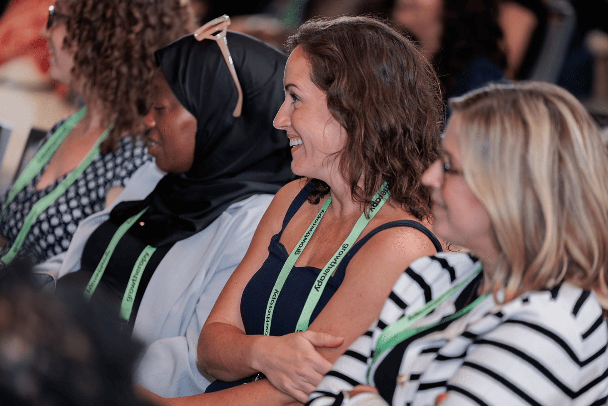 Attendees wearing Grow Therapy lanyards smile and listen during a group session at a professional event.