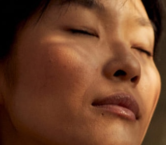 A serene close-up of a person's face with eyes closed, softly lit, conveying a calm and peaceful emotion. The warm tones add to a tranquil atmosphere.