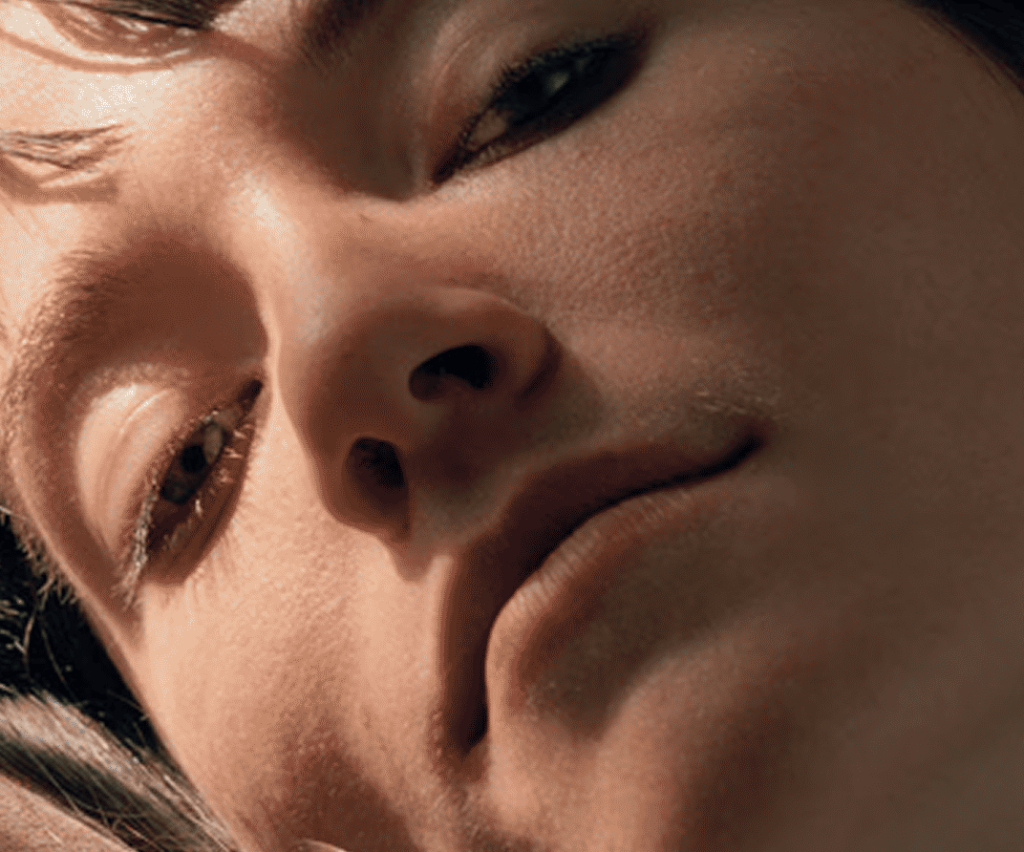 Close-up of a person's face at an angle, highlighting a serene expression and smooth skin. Soft lighting creates a calm and intimate mood.